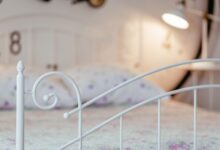 A serene bedroom featuring a white metal bed frame with floral bedding and soft lighting.