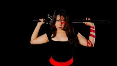 Fierce female warrior in cosplay with sword and face paint, poised against a black background.