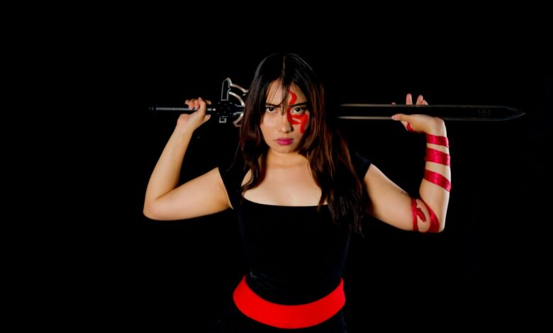 Fierce female warrior in cosplay with sword and face paint, poised against a black background.