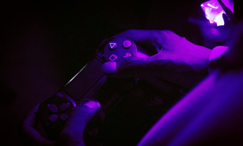 A close-up shot of hands gripping a gaming controller, illuminated by purple light, creating a vibrant atmosphere.
