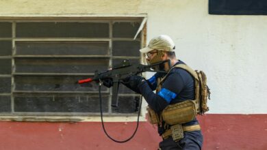 Person engaging in tactical training with an airsoft gun, wearing protective gear, in an outdoor setting.