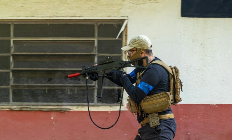 Person engaging in tactical training with an airsoft gun, wearing protective gear, in an outdoor setting.
