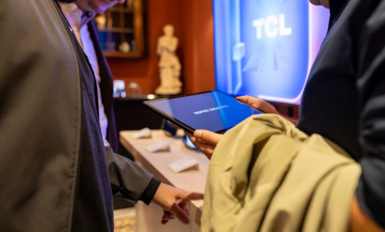 Close-up of individuals exploring a tablet device at a tech exhibit by TCL, highlighting interaction and modern technology.
