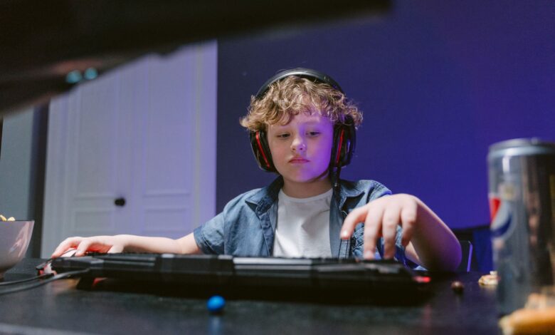 Young boy engrossed in gaming, wearing headphones, in a dimly lit room. E-sports vibe.