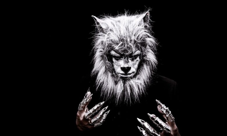 Striking portrait of an adult in a realistic werewolf costume with metallic claws against a black background.