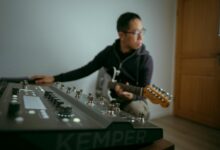 Musician playing electric guitar in a studio with a synthesizer setup in Colmar, France.