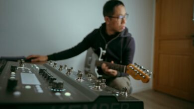 Musician playing electric guitar in a studio with a synthesizer setup in Colmar, France.