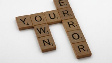 Wooden Scrabble tiles forming the motivational phrase 'Own Your Error' on a white background.