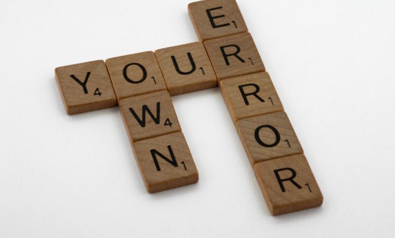 Wooden Scrabble tiles forming the motivational phrase 'Own Your Error' on a white background.