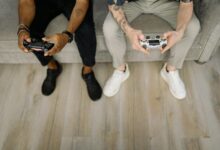 Two friends with gaming controllers focusing on a video game indoors from above.