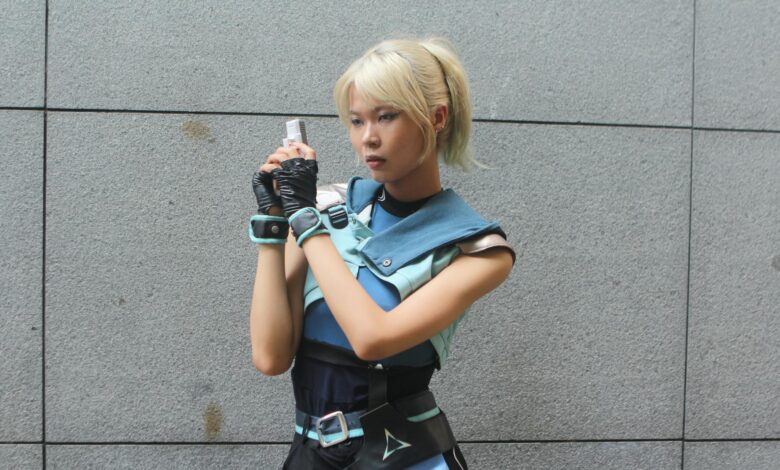 Cosplayer dressed in a futuristic outfit poses against a gray wall outdoors, exuding a sci-fi style.