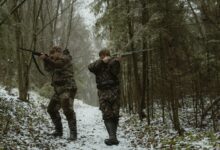 Hunters aiming their rifles in a snowy forest with camouflage gear.