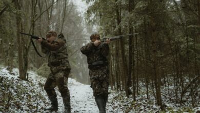 Hunters aiming their rifles in a snowy forest with camouflage gear.