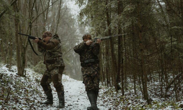 Hunters aiming their rifles in a snowy forest with camouflage gear.