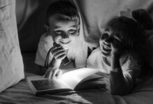Two children enjoying bedtime storytelling under a blanket fort with a flashlight.