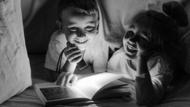 Two children enjoying bedtime storytelling under a blanket fort with a flashlight.
