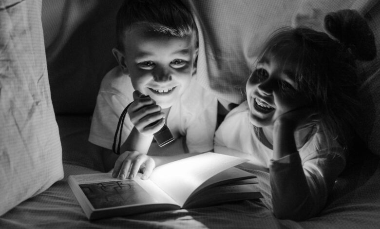 Two children enjoying bedtime storytelling under a blanket fort with a flashlight.