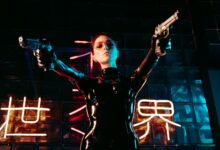 A performer in a sleek leather costume poses dramatically, holding guns under neon lights.