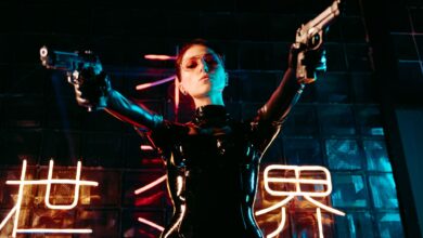 A performer in a sleek leather costume poses dramatically, holding guns under neon lights.
