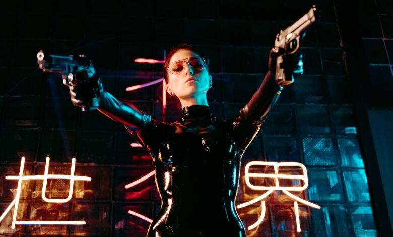 A performer in a sleek leather costume poses dramatically, holding guns under neon lights.