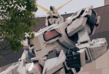 Low-angle shot of the iconic Gundam statue in Tokyo, surrounded by trees, symbolizing modernity.