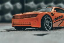 Orange contemporary toy car with sticker placed on dusty floor in soft focus