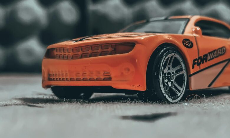 Orange contemporary toy car with sticker placed on dusty floor in soft focus