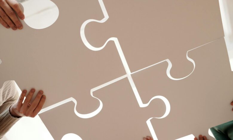 Hands of diverse individuals holding large puzzle pieces, symbolizing teamwork and unity.