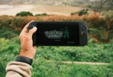 A person holds a handheld gaming device outdoors with Pokémon Legends on screen.