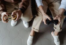 Two adults playing video games with controllers while seated on a sofa, having fun indoors.