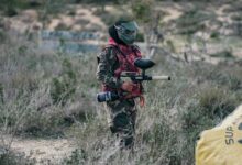 A paintball player wearing camouflage and protective gear, ready for action outdoors.