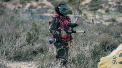 A paintball player wearing camouflage and protective gear, ready for action outdoors.
