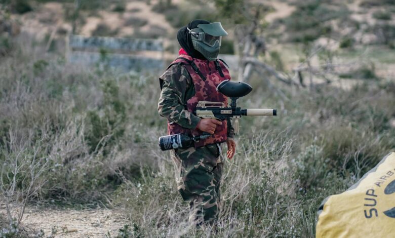 A paintball player wearing camouflage and protective gear, ready for action outdoors.