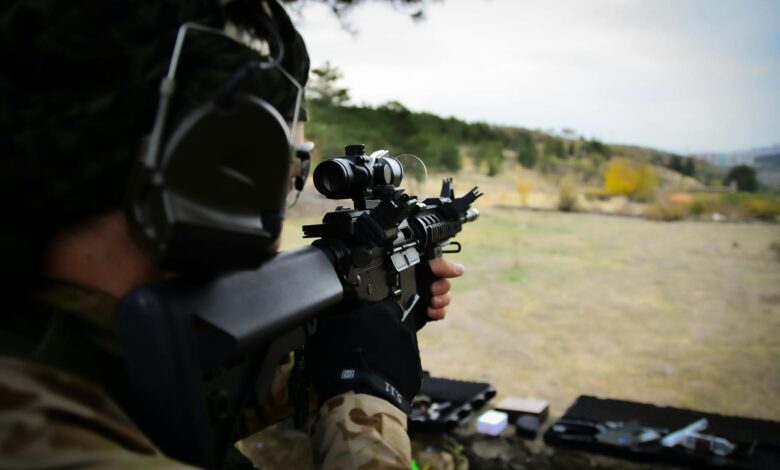 A soldier wearing camouflage and headphones aiming a rifle during outdoor target practice session.