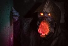 A menacing monster with glowing eyes and mouth in detailed horror cosplay peeking from a shadowy corner.