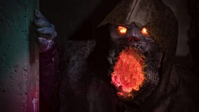 A menacing monster with glowing eyes and mouth in detailed horror cosplay peeking from a shadowy corner.