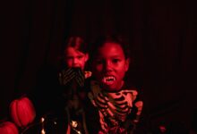 Two kids in skeleton costumes with vampire teeth and pumpkins, perfect for Halloween-themed visuals.