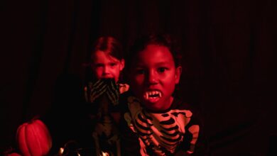 Two kids in skeleton costumes with vampire teeth and pumpkins, perfect for Halloween-themed visuals.