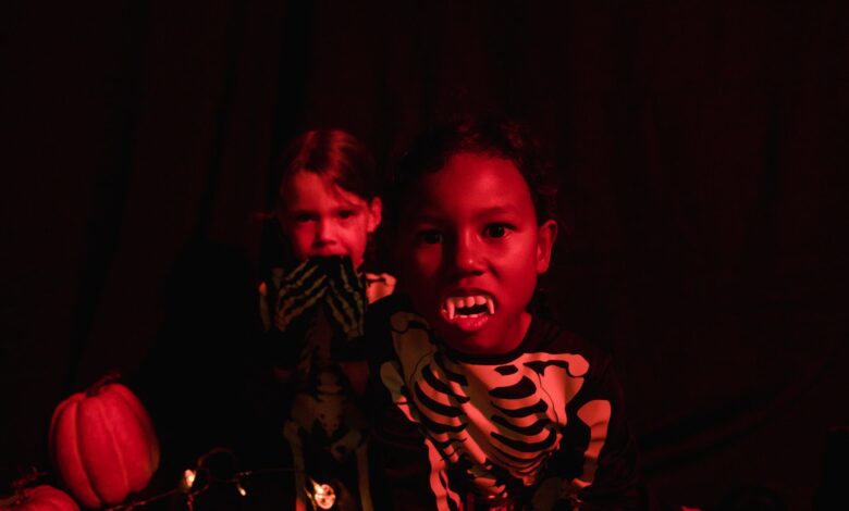 Two kids in skeleton costumes with vampire teeth and pumpkins, perfect for Halloween-themed visuals.