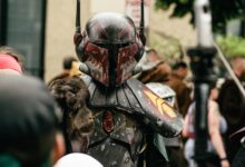 Person in detailed futuristic armor costume at a crowded outdoor cosplay event.