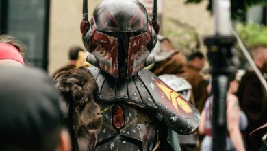 Person in detailed futuristic armor costume at a crowded outdoor cosplay event.