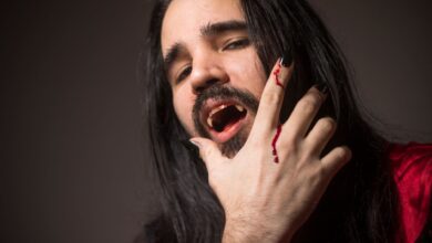 Close-up portrait of a man in vampire cosplay with fangs and bloodied hand.