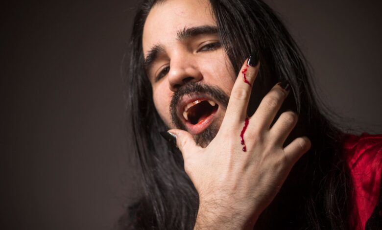 Close-up portrait of a man in vampire cosplay with fangs and bloodied hand.
