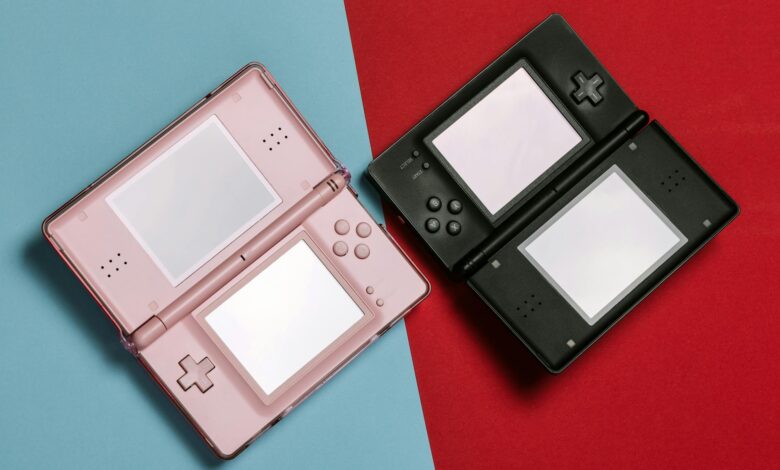 Pink and black Nintendo DS consoles displayed on contrasting red and blue backgrounds.