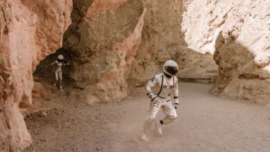 Two astronauts in space suits exploring a barren desert canyon, resembling Mars.