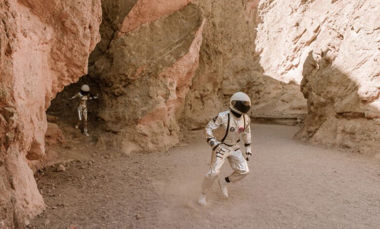 Two astronauts in space suits exploring a barren desert canyon, resembling Mars.