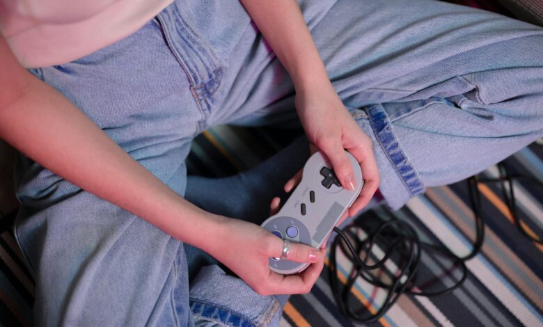 Close-up of a young woman holding a retro game controller indoors, enjoying gaming.