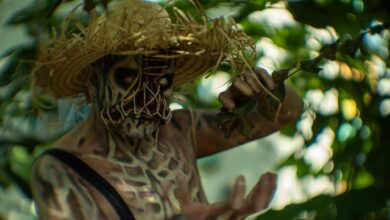 A person in halloween costume with skull makeup and straw hat in a lush outdoor setting.