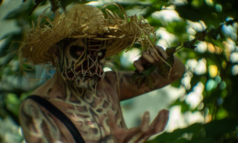 A person in halloween costume with skull makeup and straw hat in a lush outdoor setting.