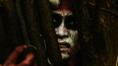 Scary demon-like face with stage makeup peeking through branches in a dark forest.